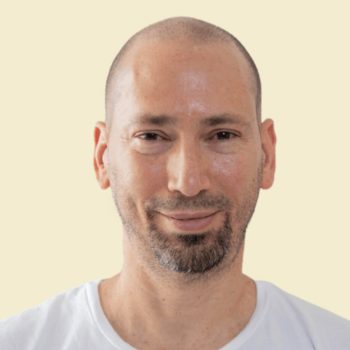 Arezky sonriente con barba y camiseta blanca sobre fondo claro